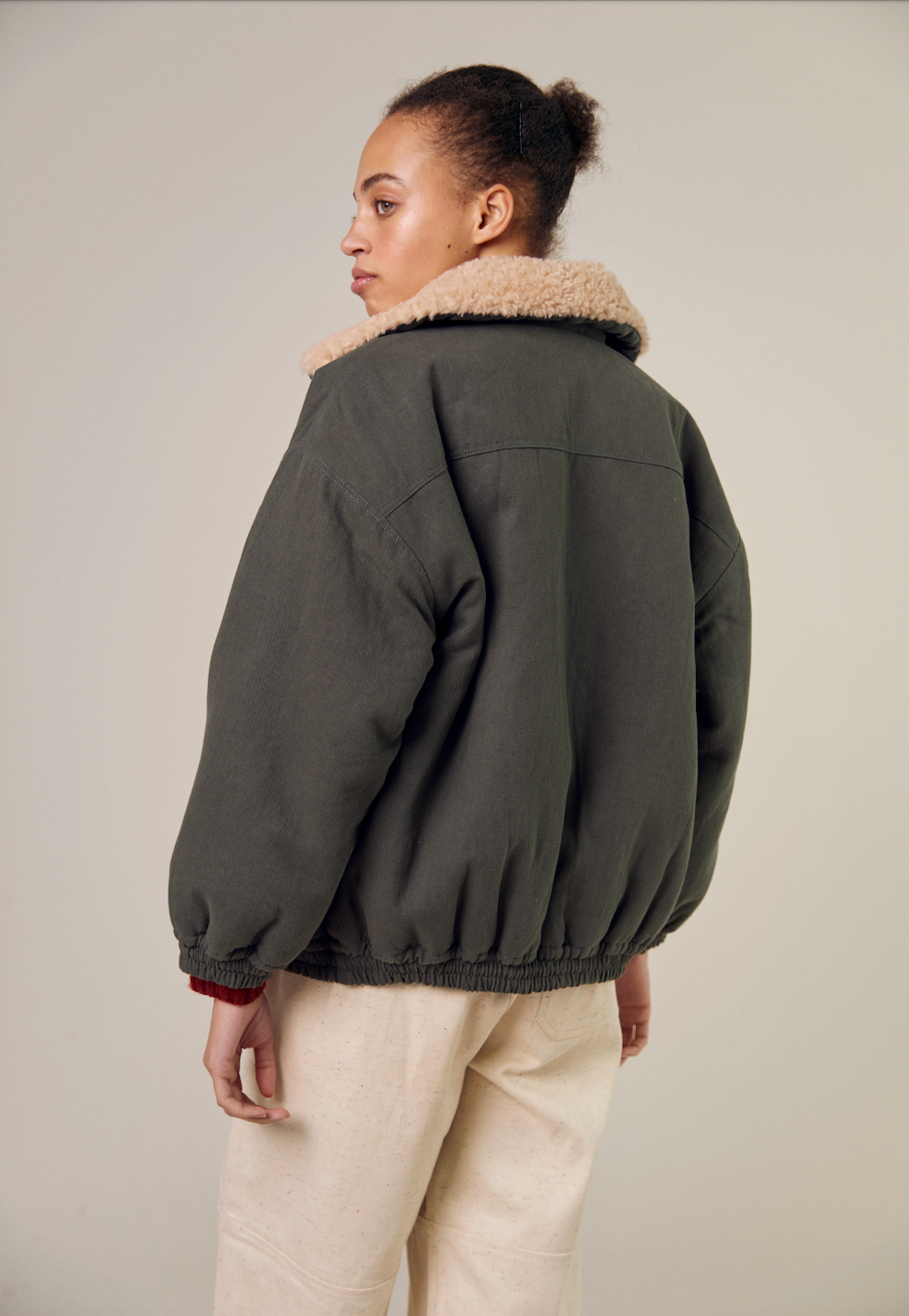 A close-up of the Sideline Wilma Jacket worn with the olive cotton twill side facing outward. The model showcases the jacket's sleek exterior, highlighting the zip front closure and rounded collar. The design emphasizes the stylish and practical aspects of the jacket, perfect for winter outings.