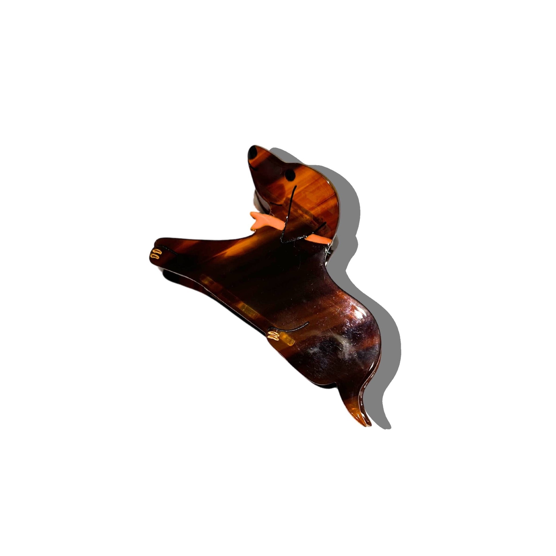 A dachshund-shaped hair claw in a rich tortoiseshell pattern, showcasing the distinctive silhouette of the dog with a pointed snout and floppy ears. The clip is accented with a small orange bow, and it casts a shadow against a white background.