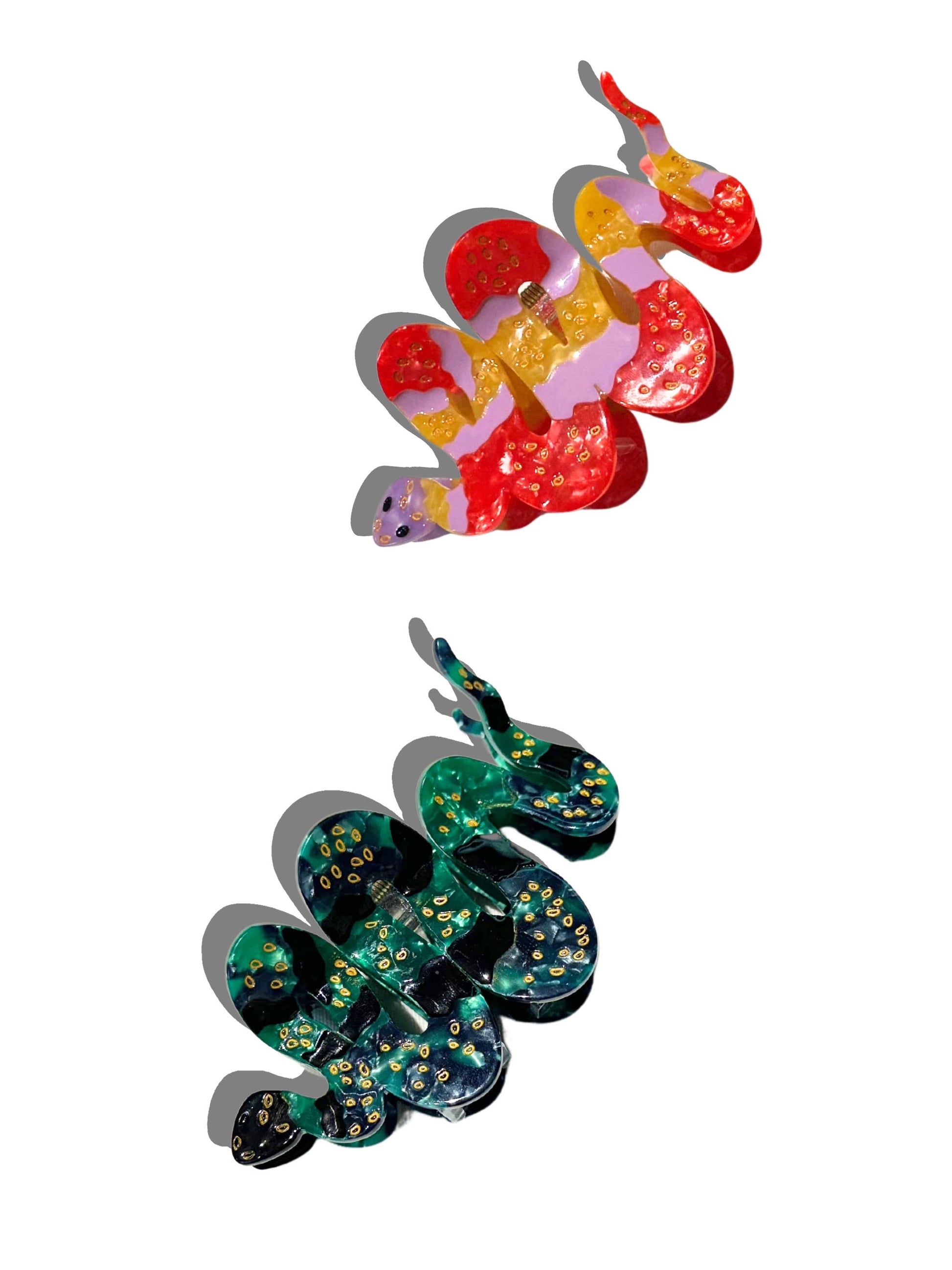 Two hand-painted snake-shaped hair claw clips, one in deep green and black with gold detailing, and the other in a vibrant mix of red, pink, and yellow. Both clips are displayed on a white background, casting soft shadows.