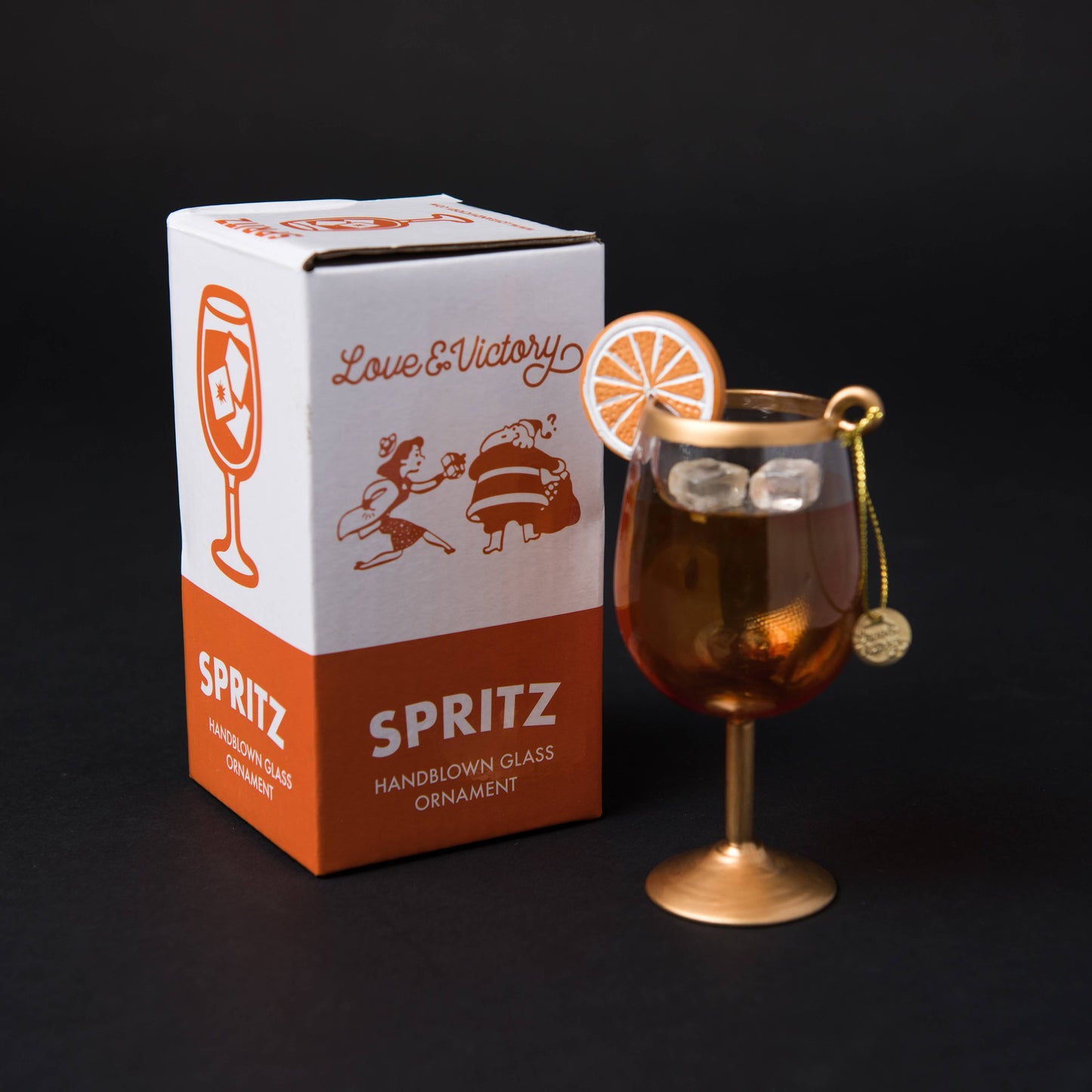 Hand-blown glass Aperol Spritz ornament featuring frosty ice and a hand-painted orange wheel garnish, measuring 4.75" x 2.5". Packaged in a custom retro holiday box.