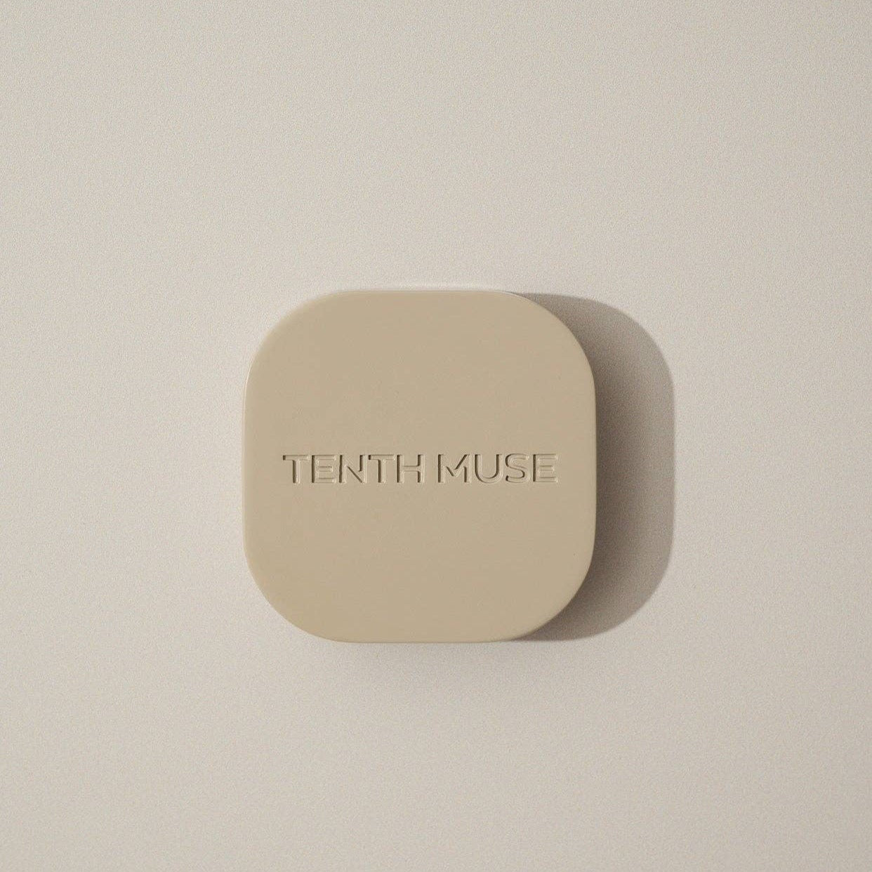 An overhead shot of the clay square refillable compact for the tenth muse solid perfume balms that has 'TENTH MUSE' lightly carved into the compact. 