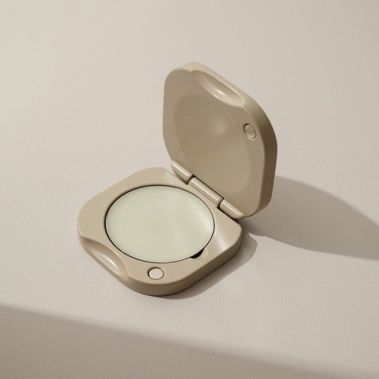 Inside a clay square refillable compact for the tenth muse solid perfume balms that has one of the solid perfume balms inside of it. 
