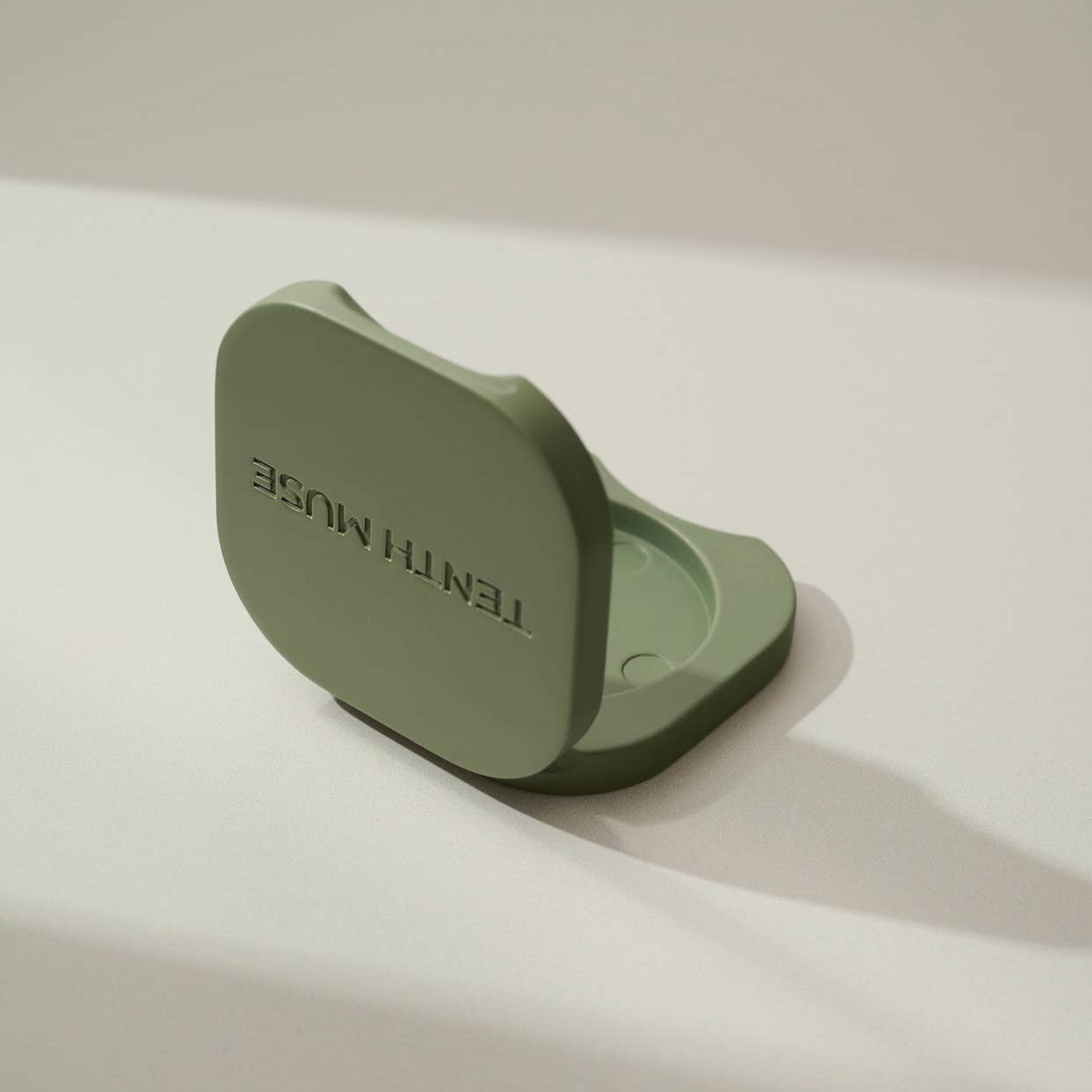 A halfway open green/matcha square refillable compact for the tenth muse solid perfume balms that has 'TENTH MUSE' lightly carved into the compact and shows the hole in which the solid perfume balm goes inside of. 