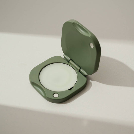 Inside a green/matcha square refillable compact for the tenth muse solid perfume balms that has one of the solid perfume balms inside of it. 