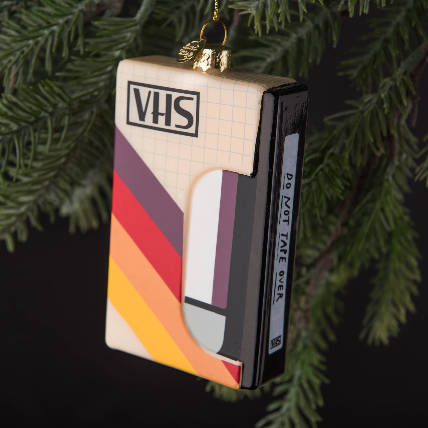 Hand-blown glass VHS Tape ornament with a hand-painted slipcase and "do not tape over" sticker detail, hanging from a christmas tree branch