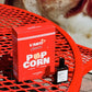 Red 'L'Anti' popcorn box on a red metal chair with a blurred background