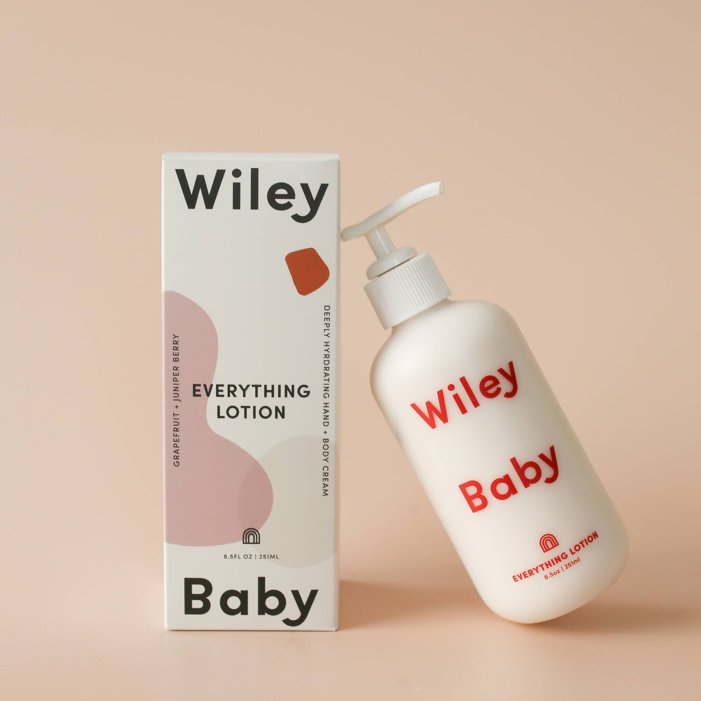 Wiley body everything lotion for baby, in a white cylindrical matte glass bottle with curved edges and a white pump cap, spelling Wiley baby in red text across the bottle, next to its packaging a cuboid cardboard box mainly white with pink, cream and red organic shapes on alongside the branding Wiley baby at the top and bottom with the name everything lotion in the middle in a smaller font