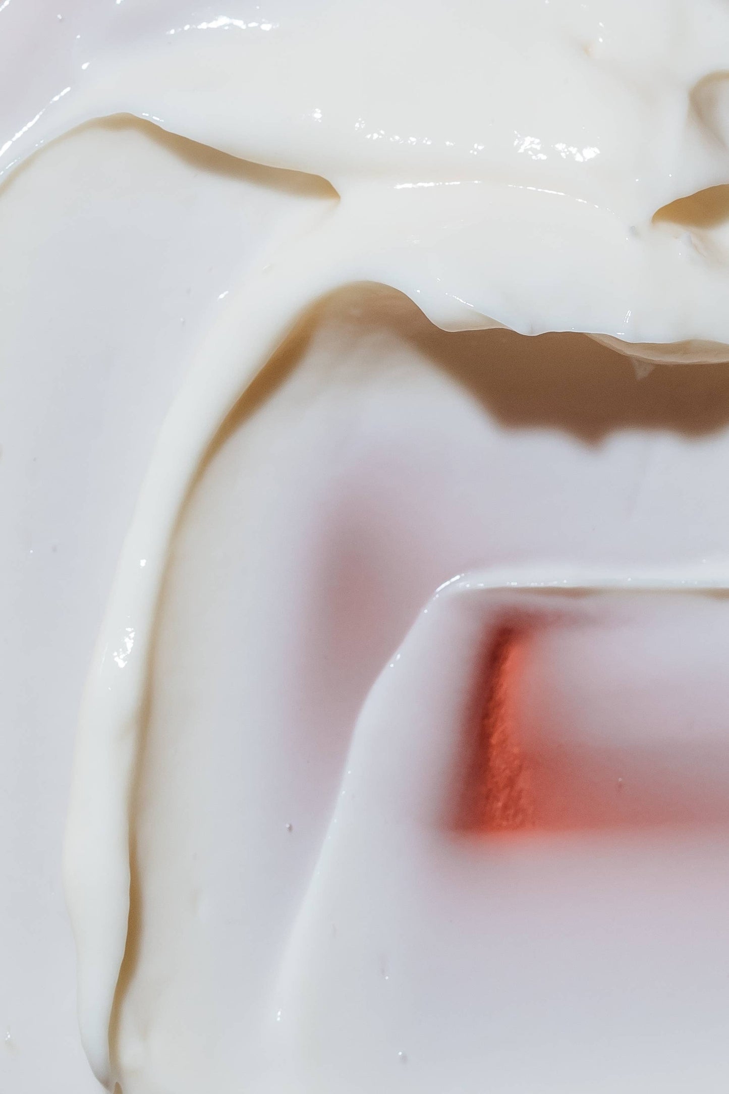 A close up of the creamy texture of the body lotion, a spatula has spread the white lotion on a rust red brick and there are multiple thick layers all together