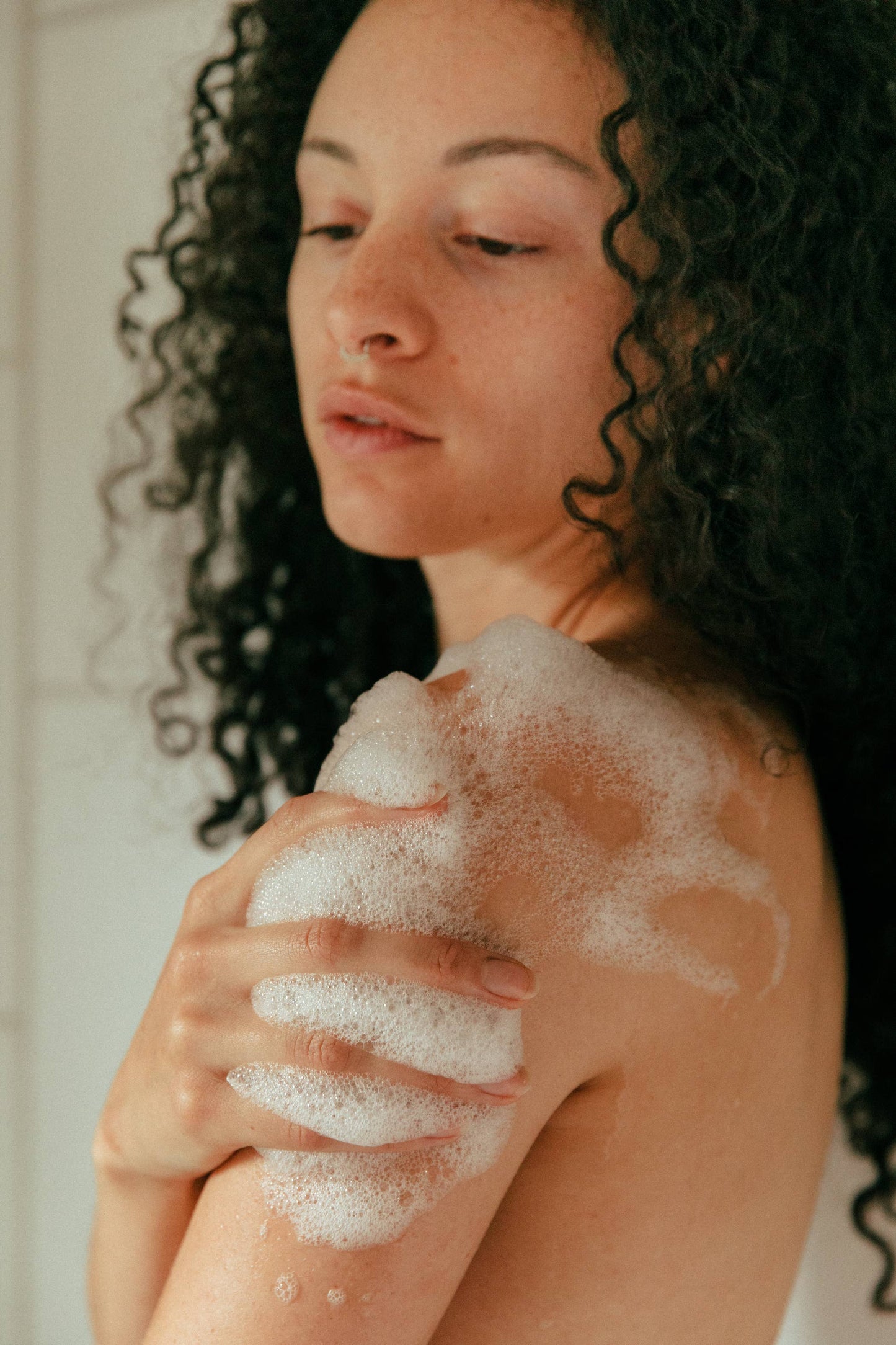 A woman with curly hair lathering baubles on her shoulder with her hand