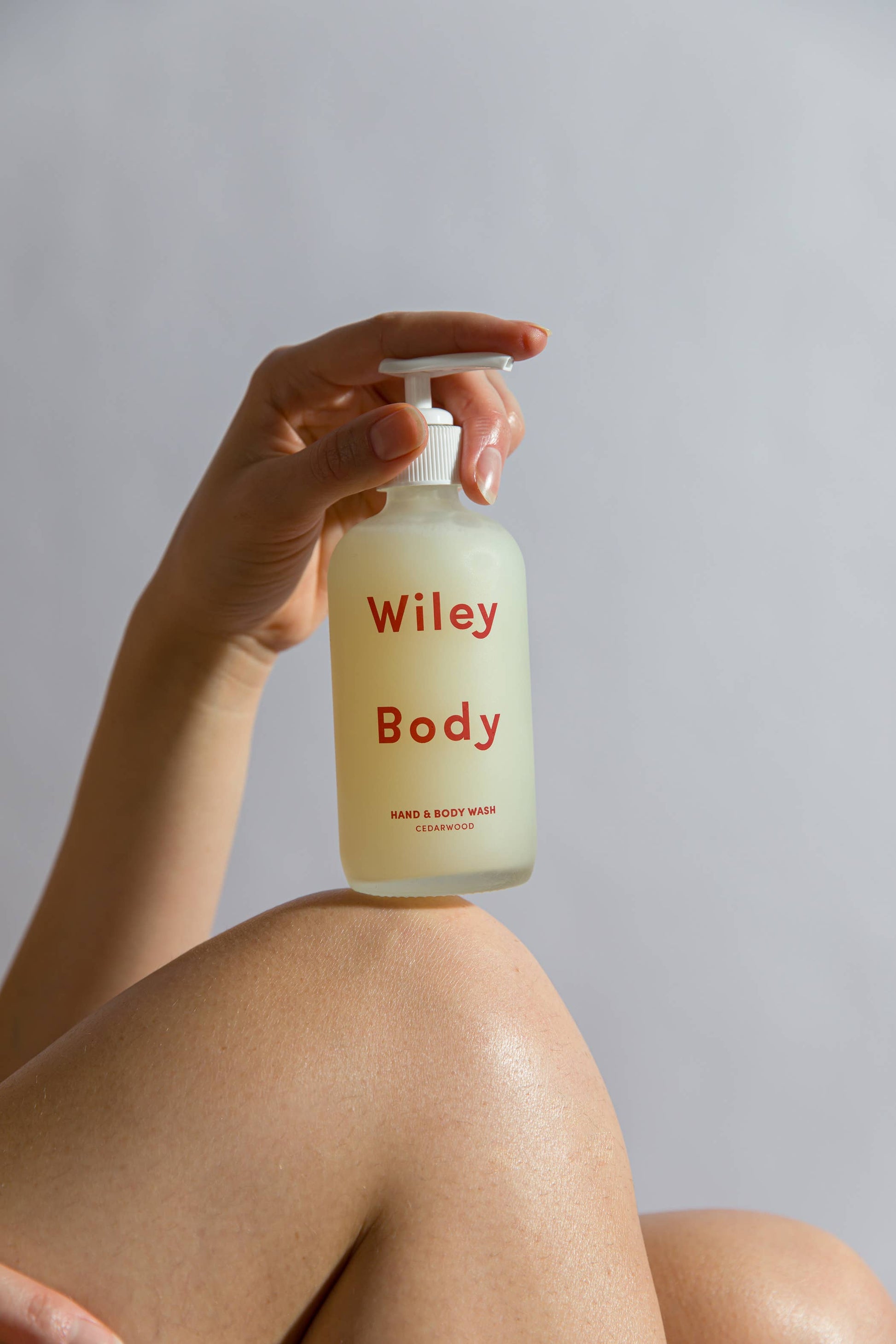 A woman’s hand holding the pump of the Wiley body hand and body wash bottle on top of her knee