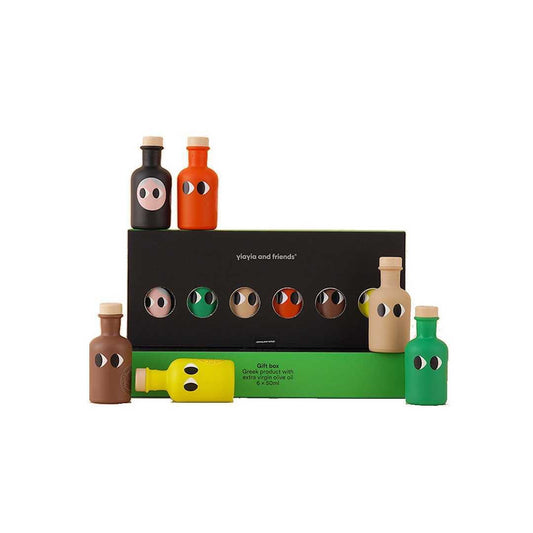 Yiayia and Friends Extra Virgin Olive Oil Gift Set featuring six mini bottles in bold, playful colours with quirky eye illustrations. The set includes basil, garlic, chilli, lemon, black truffle, and classic extra virgin olive oil, packaged in a stylish black and green box with cut-out windows displaying the bottles inside.