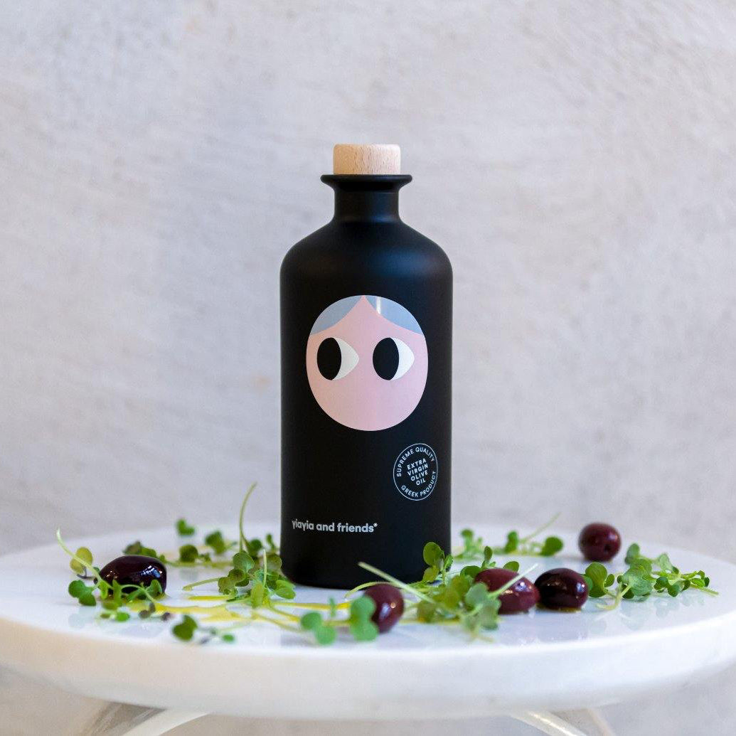 Black bottle with a pink face design on a white surface with greenery