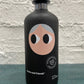 Black bottle with a face design on a textured surface and light gray background