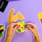 Hands assembling a cheeseburger model with a drink on a purple background