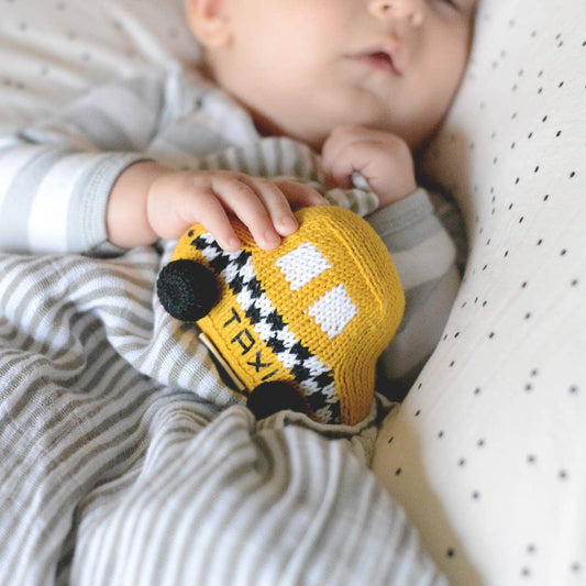 Baby holding a knitted taxi toy with a soft focus background