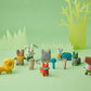 On a bright green backdrop with trees and grass paper cutouts. All of the small Donna Wilson knitted toys grouped together, from left to right is the lion, mole, rabbit, peanut, fox, cat, little trees, snail, raccoon and horse