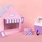 Pink and purple toy house with striped awning and matching car on a pink background