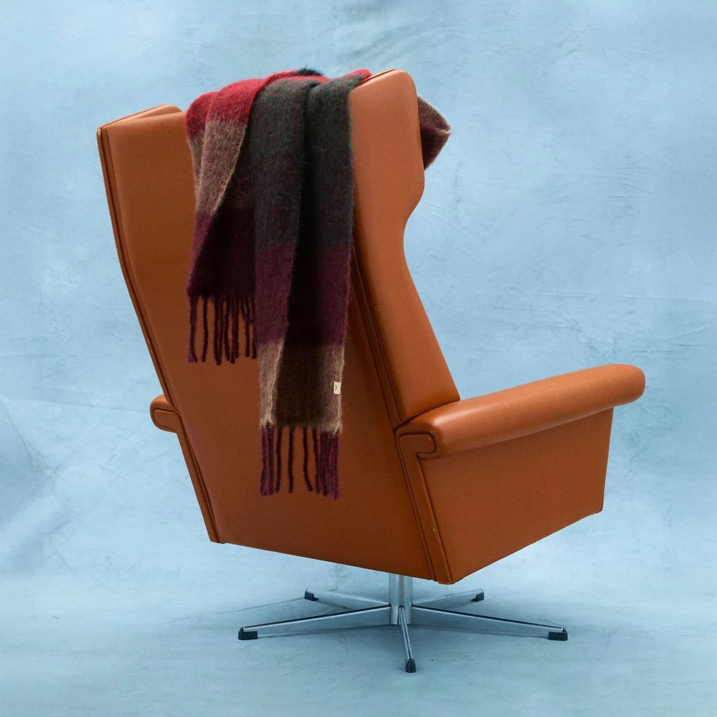 Orange armchair with a plaid scarf draped over it on a light blue background