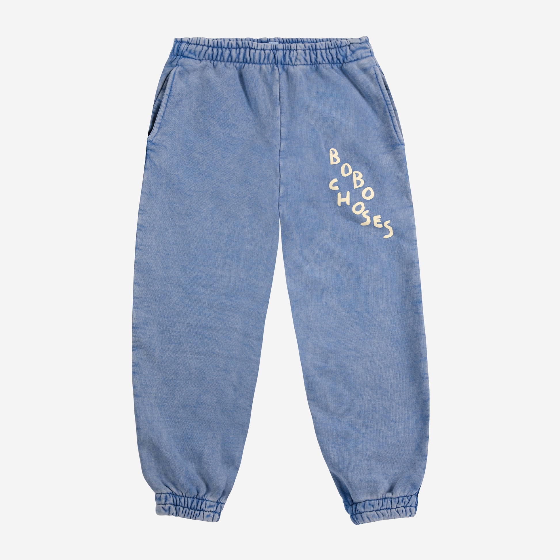 A pair of children's jogger-style sweatpants in a washed blue colour, laid flat against a white background. They feature an elasticated waistband and cuffs, side pockets, and a playful "BOBO CHOSES" logo in an irregular font on the upper left leg. The fabric has a slightly faded, vintage-inspired look.