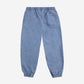 A pair of children's jogger-style sweatpants in washed blue, laid flat with the back side facing up. They feature an elasticated waistband and cuffs, a single square patch pocket on the right side, and a relaxed fit. The fabric has a soft, slightly faded look for a vintage-inspired feel.