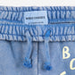 A close-up of the waistband of a pair of washed blue sweatpants, featuring an elasticated band with a gathered texture and a matching drawstring with knotted and frayed ends. A light blue fabric label sewn inside the waistband displays the brand name "BOBO CHOSES" along with the size "6-7 YEARS, 122 CM." Part of the "BOBO CHOSES" logo print is visible on the right side.