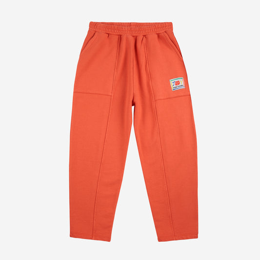 A frontal view of the orange sweatpants laid flat, showing their elastic waistband, stitched details, and the small pocket with a Bobo Choses logo patch.