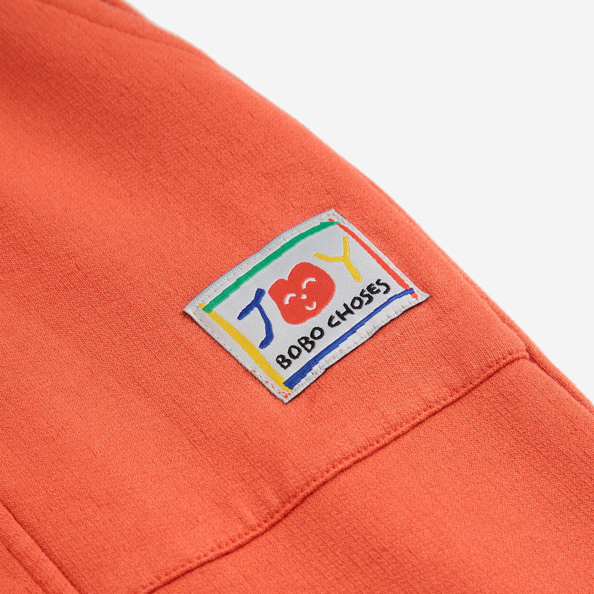 A close-up of the sweatpants’ side pocket, which has a colourful, playful "JOY" logo patch from Bobo Choses.