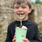 Child holding a green cup with a straw and cherry, outdoors.