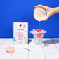 Soap maker kit with packaging and a hand pouring liquid into a mold against a blue background