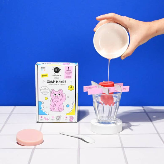 Soap maker kit with packaging and a hand pouring liquid into a mold against a blue background