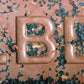Close-up of a chocolate bar with 'B' branding, surrounded by green seeds.