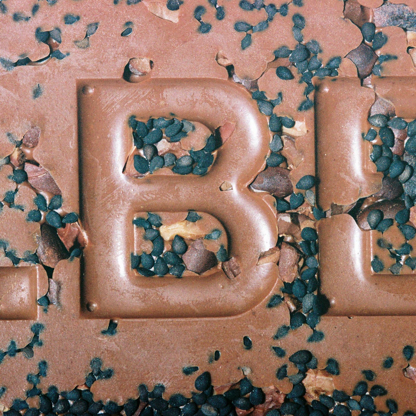 Close-up of a chocolate bar with 'B' branding, surrounded by green seeds.