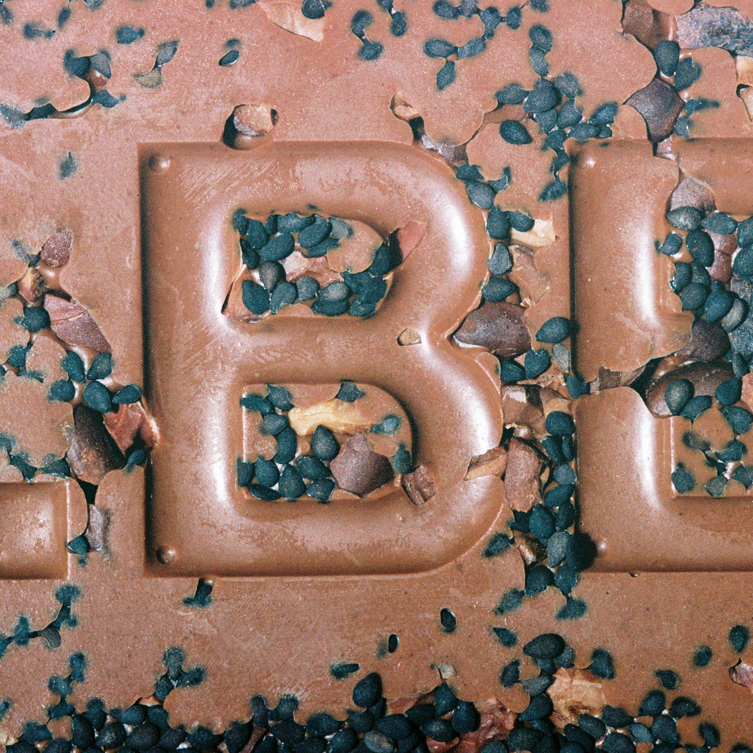 Close-up of a chocolate bar with 'B' branding, surrounded by green seeds.