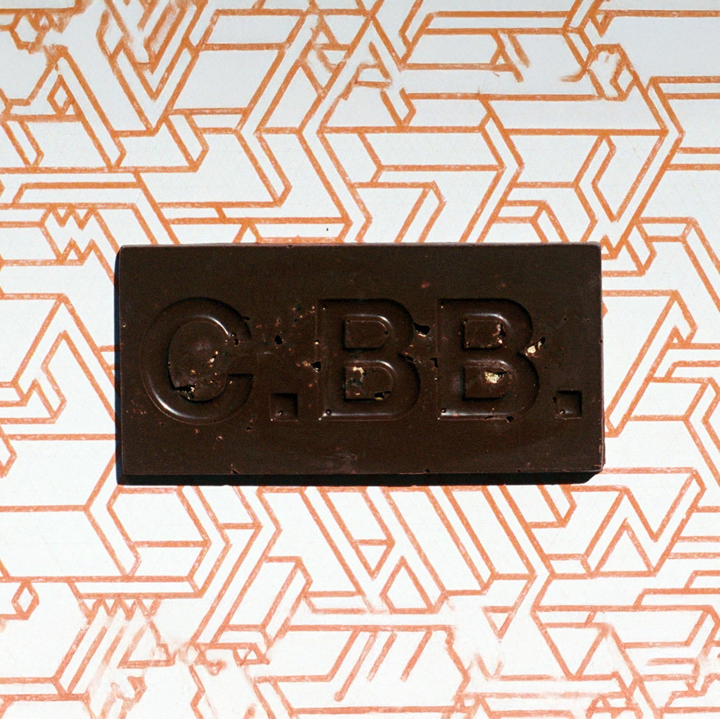 Dark chocolate bar with 'C.B.B.' branding on a geometric patterned background