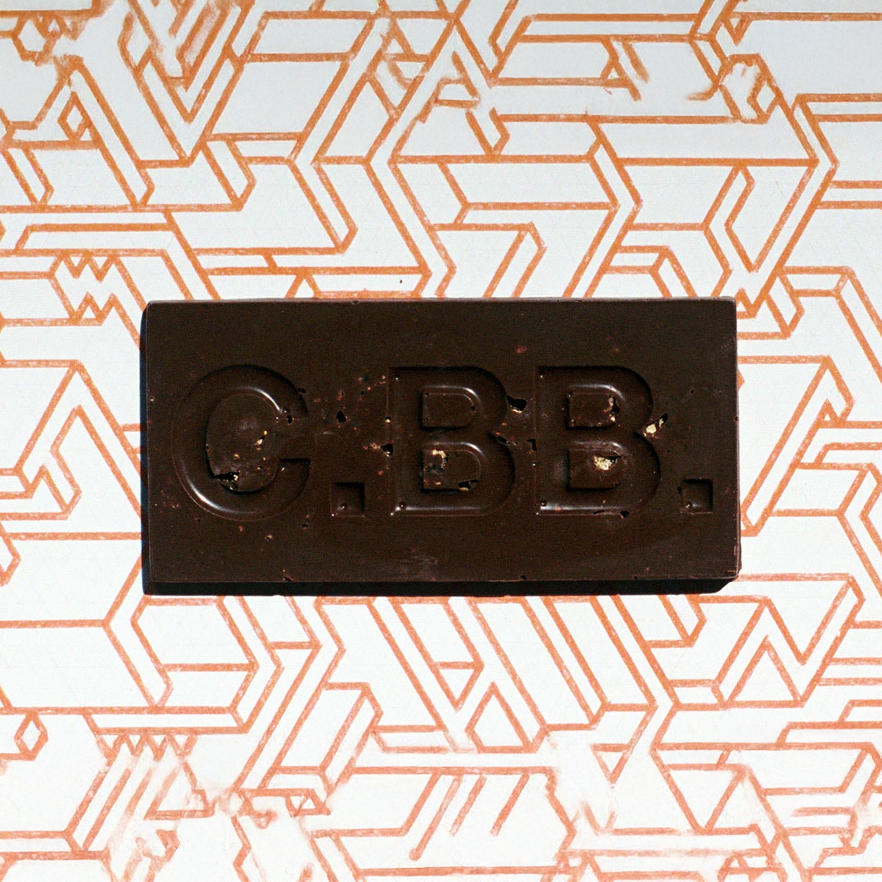 Dark chocolate bar with 'C.B.B.' branding on a geometric patterned background