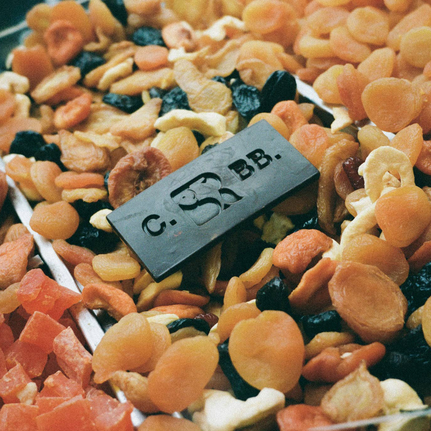 Close-up of dried fruits and nuts, featuring a small rectangular object with 'C.S.' and 'B.B.' on top.