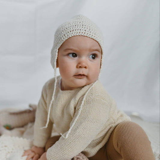 Baby wearing a knitted bonnet and scarf on a white background