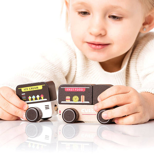 A child wearing a white top playing with wooden toy cars on a reflective surface