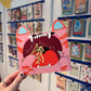 Person holding a pink cat-shaped birthday card with a colorful background of more cards.