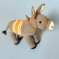 Knitted donkey toy with a striped saddle on a light blue background
