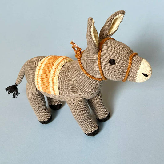 Knitted donkey toy with a striped saddle on a light blue background