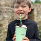Child holding a mint green cup with a straw and cherry, outdoors.