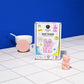 Soap maker packaging with a pink cat design on a tiled surface against a blue wall.
