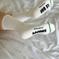 White socks with black text worn on a white bedspread