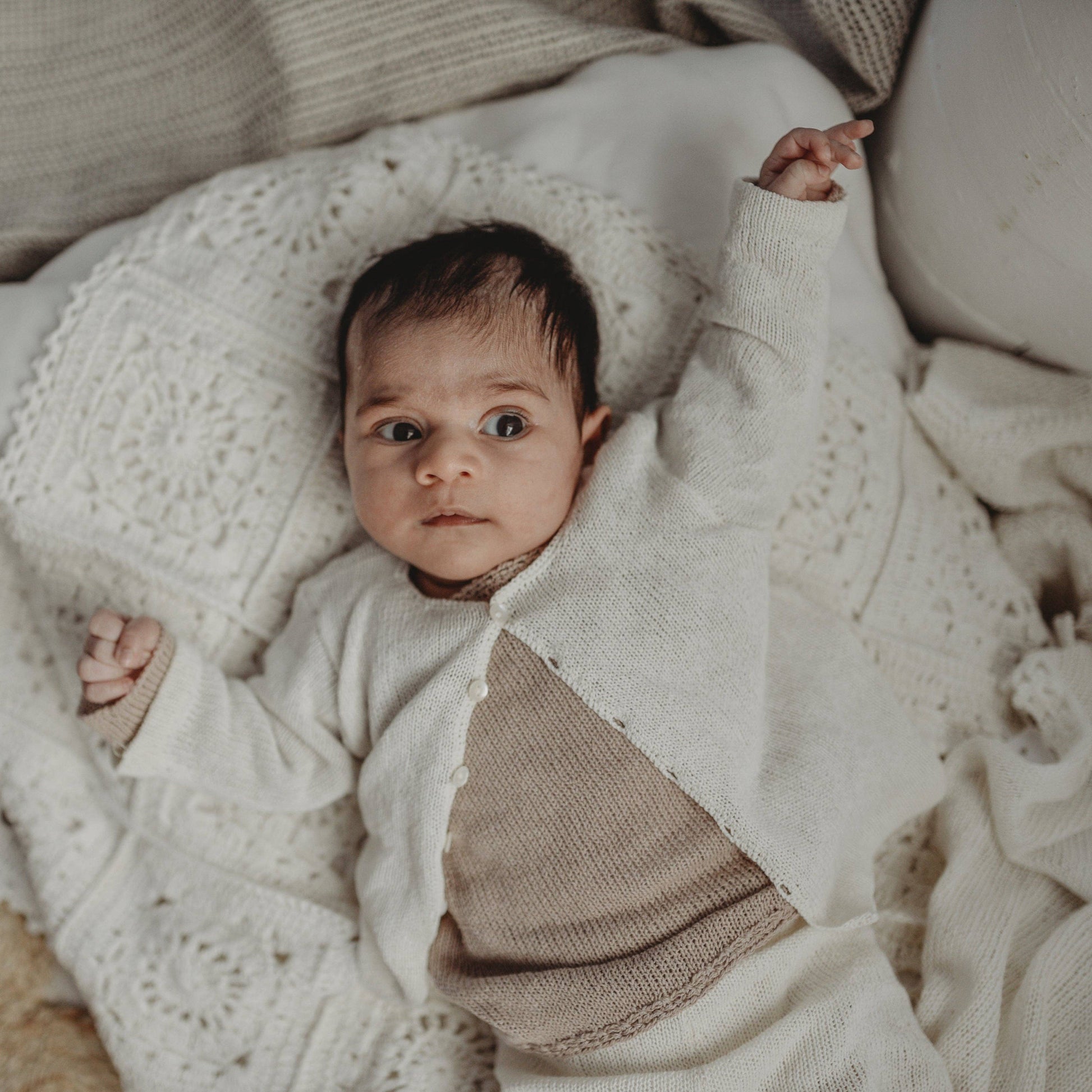 Baby wrapped in a white knit blanket with a neutral background