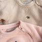 Close-up of two fleece jackets with embroidered designs on a neutral background