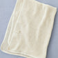 on a grey blue backdrop the fog line blanket is folded into a rectangle, showing the waffle texture of the cream yarn