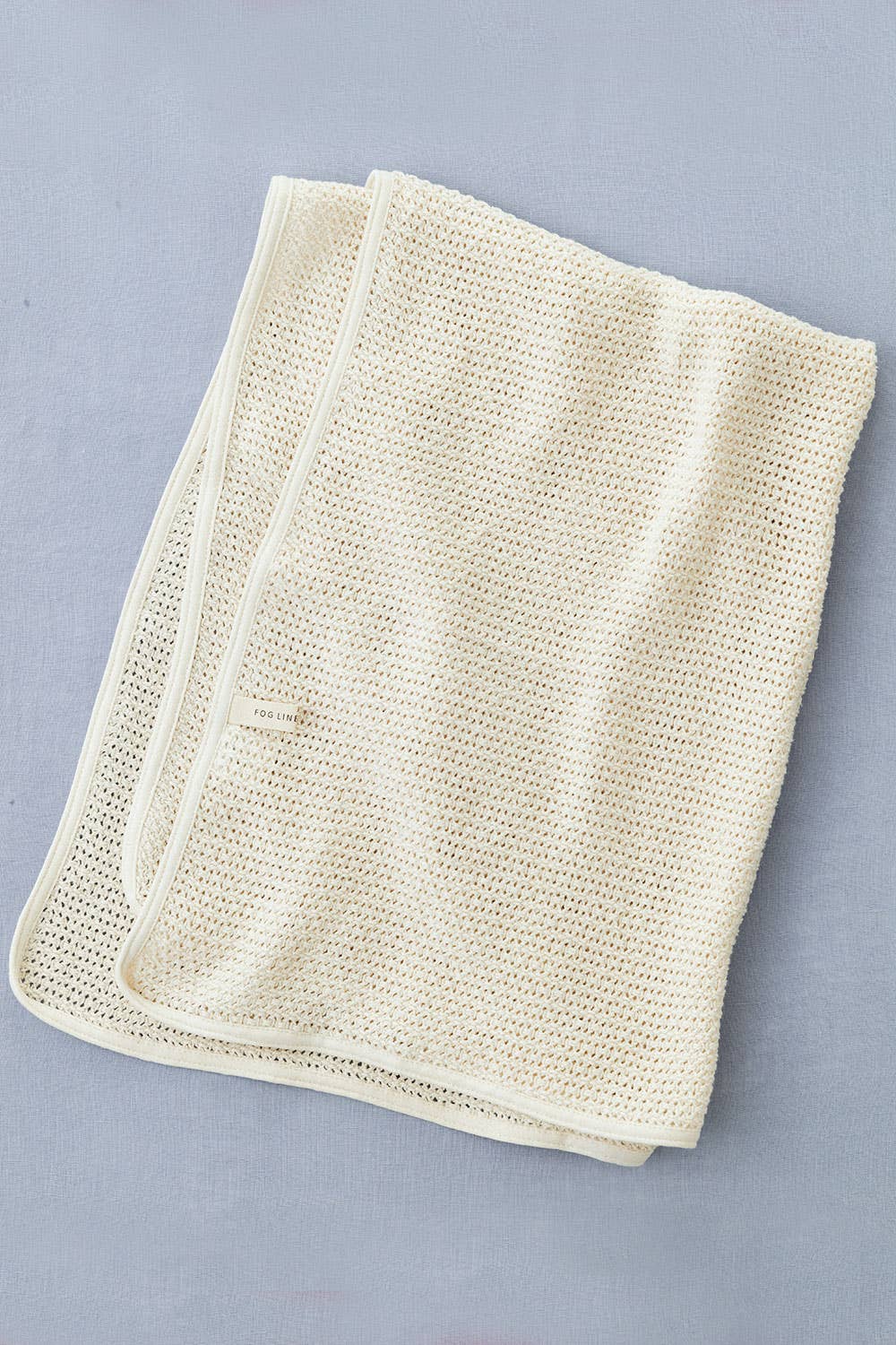 on a grey blue backdrop the fog line blanket is folded into a rectangle, showing the waffle texture of the cream yarn