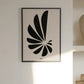 An image depicting the Hotel Magique Shell A3 print. The print depicts the imprint of a shell in black. The background is beige. The print is framed with a black border. The frame is hung against a white wall