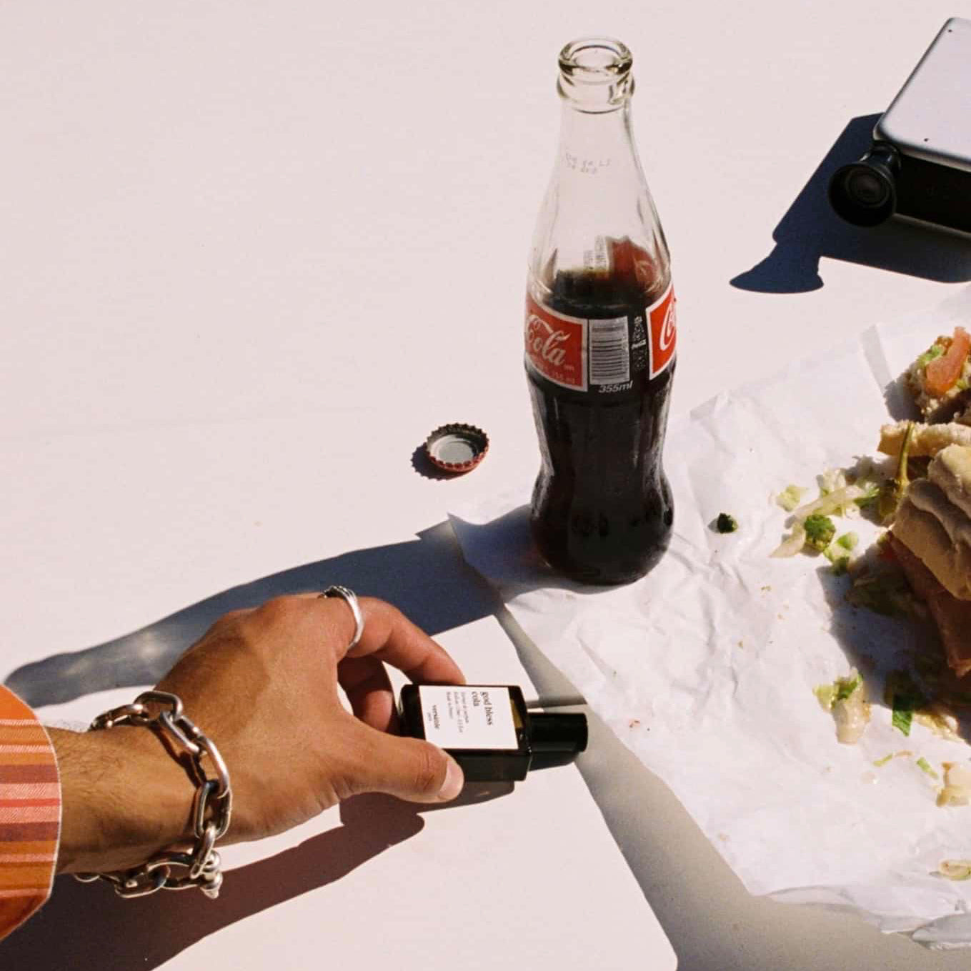 Person holding a bottle of Coca-Cola next to a bottle cap on a white surface.